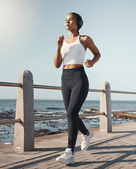 Fitness, woman run at beach and with headphones listening to music for health wellness. Training or exercise, marathon or sportswear and female person running along the promenade listen to radio © HockleyMedia/peopleimages.com