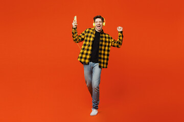 Fototapeta na wymiar Full body young cheerful happy man wear yellow checkered shirt black t-shirt headphones listen to music use mobile cell phone isolated on plain red orange background studio portrait Lifestyle concept