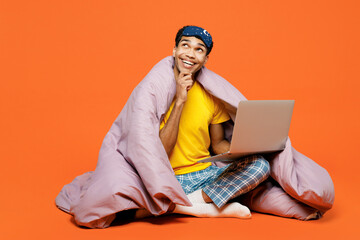Full body young IT man wear pyjamas jam sleep eye mask sit wrapped in duvet rest relax at home work...