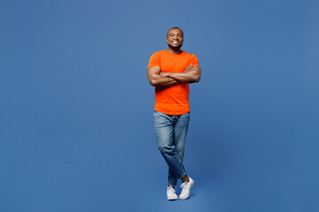 Full body fun young man of African American ethnicity he wear orange t-shirt hold hands crossed folded look camera isolated on plain dark royal navy blue background studio portrait. Lifestyle concept.