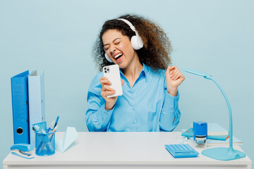 Young employee business woman wear casual shirt headphones listen to music sit work at white office...