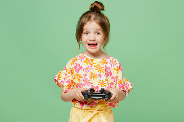 Little child kid girl 6-7 years old wear casual clothes have fun hold in hand play pc game with joystick console isolated on plain pastel green background Mother's Day love family lifestyle concept.