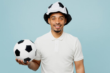 Young cheerful fun happy man fan in basic t-shirt hat looking camera cheer up support football sport team hold in hand soccer ball watch tv live stream isolated on plain pastel blue color background