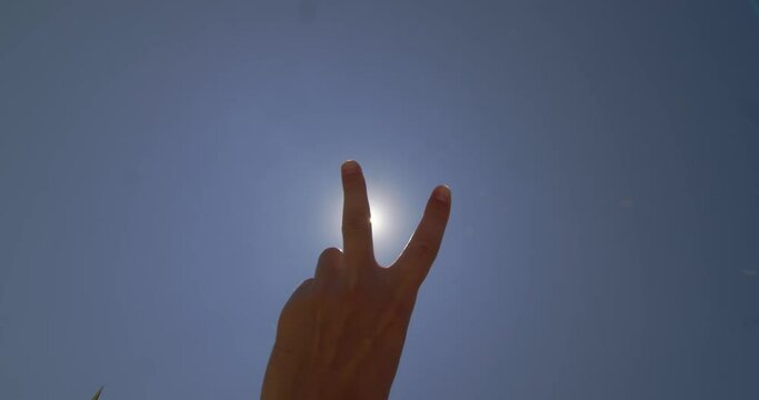 SLOW MOTION CLOSE UP DOF: Showing a victory hand gesture, raising and parting index and middle fingers, while the other fingers are clenched. Peace sign with sunny stormy cloudy sky and in background
