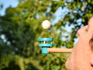 Balance concept. Young adult man balancing ball of blow pipe toy outdoors at sunrise. Beautiful nature landscape garden on background illuminated shiny bright Sun light. Closeup male face