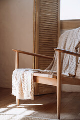 Fototapeta na wymiar Wooden armchair with cotton knitted plaid in room