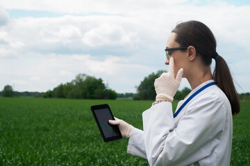 a female agronomist in a white coat checks the growth of plants in the field. A biologist in the...