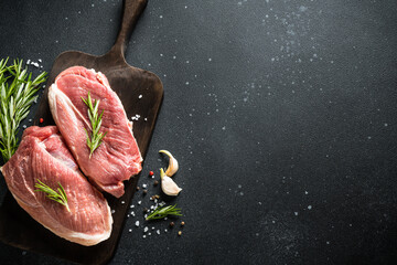 Raw meat steaks with spices at dark background. Top view with space for text.