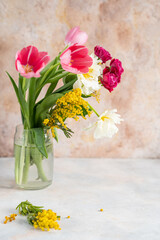 Glass vase with bouquet of beautiful tulips and mimosa in the light background