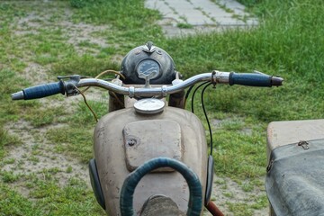 front part of old rusty classic iron with sidecar of heavy brown color retro motorcycle made in ussr on green grass outdoors in summer day