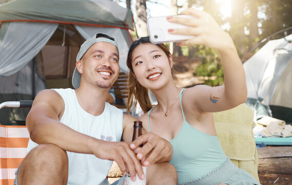 Selfie, love and young couple on a camp in the woods for a summer weekend trip or holiday. Happy, smile and man with beer while his girlfriend taking a picture in forest on outdoor vacation together.