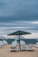 Fototapeta na wymiar Sun bed chairs with matress and straw beach umbrellas on beach. Blue hour time background by the sea..