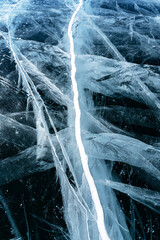 Transparent dark blue ice of frozen Baikal lake with white cracks pattern. Beautiful winter nature background with copy space.