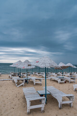 Fototapeta na wymiar Sun bed chairs with matress and straw beach umbrellas on beach. Blue hour time background by the sea..