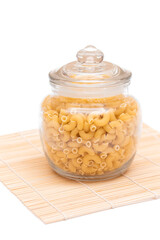 Uncooked Chifferi Rigati Pasta in Glass Jar on Bamboo Mat on White Background. Fat and Unhealthy Food. Classic Dry Macaroni. Italian Culture and Cuisine. Raw Pasta