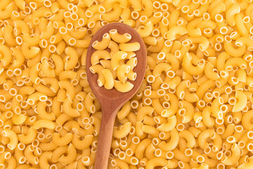 Uncooked Chifferi Rigati Pasta Background with Wooden Spoon. Fat and Unhealthy Food. Classic Dry Macaroni. Italian Culture and Cuisine. Raw Pasta