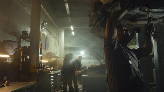 Professional auto technician working in repair shop taking wrench from the table to fix wheel part