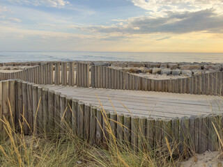 A wood pedestrian walkways, build over a sand dune that is used to give beach access in Furadouro beach, glows at sunset. Ovar, Aveiro, Portugal, Europe