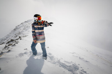 Full length shot of a cheerful skier carrying her skis on her shoulder. A skier is standing on top...
