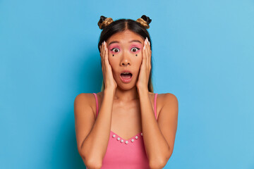 Portrait of a shocked young asian woman looking at camera isolated over blue background