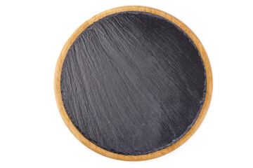 Round rustic black slate stone plate on wooden cutting board, isolated on white background.