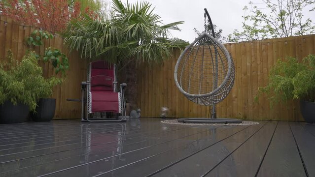 Typical English garden on a rainy day showing decking, hanging chair and palm tree