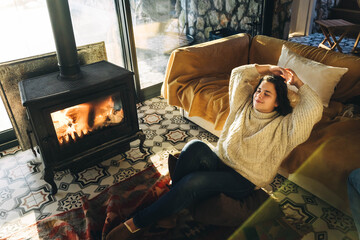 Woman in sweater has rest near the fireplace.