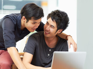 Teamwork, gay couple working with laptop and at their home together happy. Collaboration or...