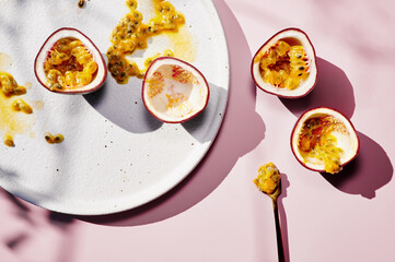 Fresh passion fruit on white ceramic plate with golden spoon. Sun light, shadows, top view. Light pink background. Summer exotic breakfast.