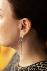 Round silver earrings on the ear of a well-groomed lady on a blue background