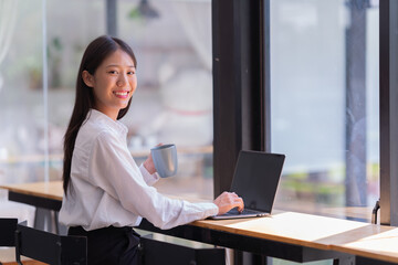 Sharing good business news. Attractive young businesswoman talking on the mobile phone and smiling while sitting at her working place in office and looking at laptop PC.