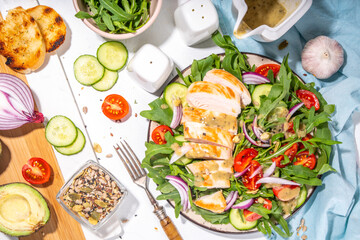 Grilled chicken fillet with vegetable salad. White meat, chicken or turkey breast, with fresh vegetables and greens salad, tomato, arugula, cucumber, onion, green olive oil sauce on white background