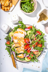 Grilled chicken fillet with vegetable salad. White meat, chicken or turkey breast, with fresh vegetables and greens salad, tomato, arugula, cucumber, onion, green olive oil sauce on white background