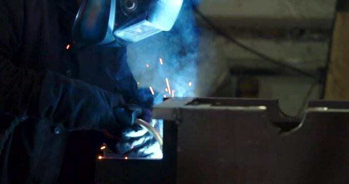 Slow motion 4k footage of a worker welds metal in a protective helmet. Heavy industry and metallurgy. Professional at work. Industrial electrogas welding.