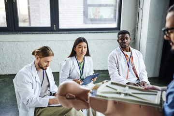 medical training, diverse group of multiethnic students in white coats looking at paramedic standing with CPR manikin on blurred foreground, acquiring and practicing life-saving skills concept