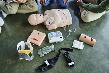 cropped view of multiethnic participants of first aid seminar near CPR manikin, defibrillator,...