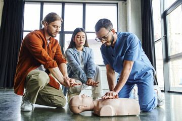 professional paramedic in eyeglasses and uniform showing chest compressions on CPR manikin near...