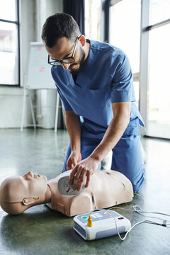 first aid training seminar, young medical instructor in uniform and eyeglasses applying defibrillator pads on CPR manikin, cardiac resuscitation, health care and life-saving techniques concept