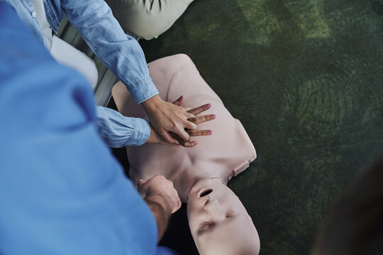 first aid seminar, top view of young woman practicing life-saving skills while doing chest compressions on CPR manikin near medical instructor, emergency situations response concept, cropped view - Powered by Adobe