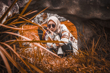 Girl wearing hijab sitting and frowning on the other side of the rock