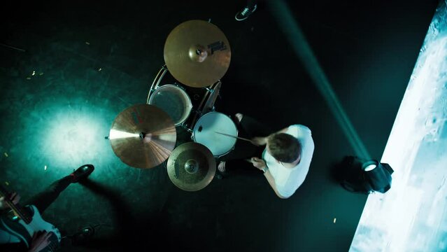 Jib shot of a drummer performing his solo during rock band concert on stage of a large venue, surrounded by bright flashing stage lights