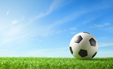 Close-up football ball on green grass with blue sky  background.