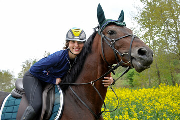 Purebred horse with rider on a rapeseed field outdoors in rural scene