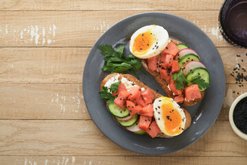 Healthy sandwich with bread or toast, smoked salmon, soft egg, cream cheese, cucumber, radish, black sesame and parsley on old wooden table. Delicious protein fish sandwich for breakfast. Smorrebrod.
