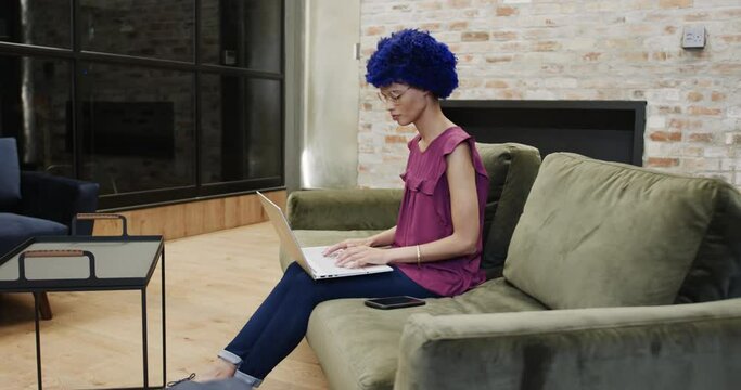 Biracial businesswoman with blue afro and using laptop in office, slow motion