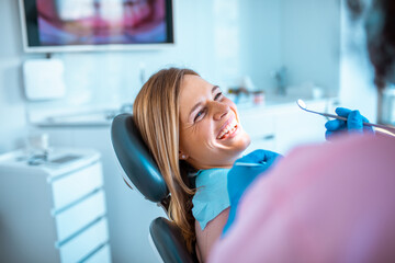 Female dentist working on a female patients teeth in her dental office - obrazy, fototapety, plakaty