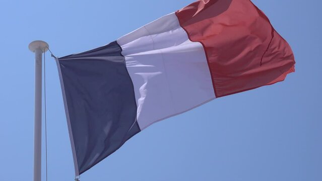 France national flag waving in the wind on a flagpole with blue sky background.