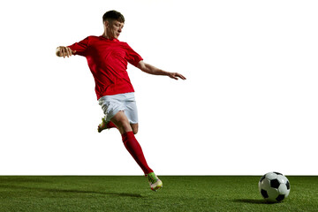 Young man in red uniform, football player in motion, playing, kicking ball on sports field against...
