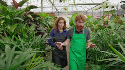 Two employees walking through isle inside plant store. man and woman staff wearing aprons, male employee explaining Flower Shop business