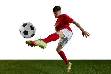 Competitive man, football player in red uniform training, kicking ball with leg against white background. Concentration. Professional sport, action, lifestyle, competition, hobby, training, ad concept